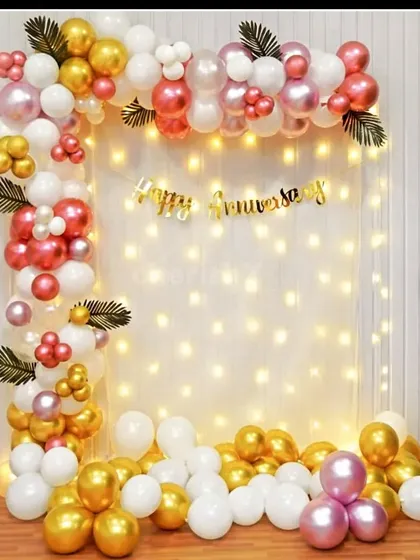 A beautiful anniversary photo corner. A backdrop of fairy lights is framed by an elegant balloon garland in white, gold, and metallic pink.