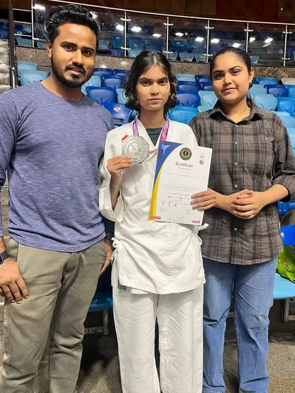 A student with her silver medal from the All India Karate Championship, standing with her coach and family. This is a team effort.
