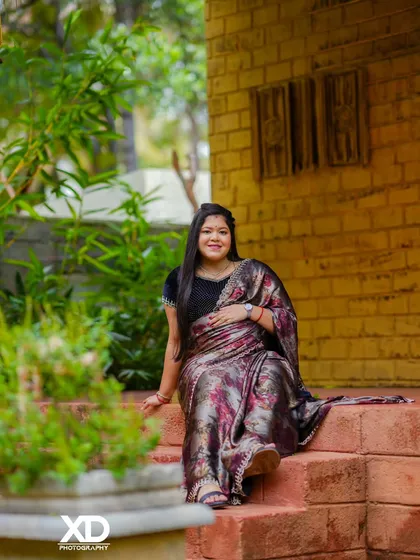 A relaxed portrait of the mother-to-be sitting on brick steps, her printed saree adding a touch of modern elegance to the rustic setting.