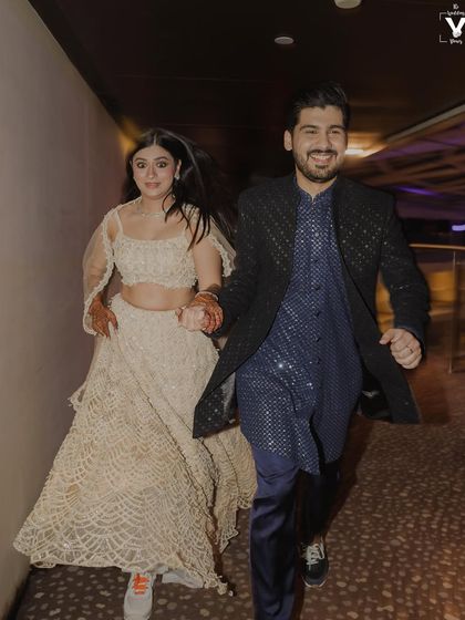 The bride and groom, in sneakers, run hand-in-hand down a corridor. This energetic and candid shot perfectly captures their fun-loving personalities and the excitement of their sangeet night.
