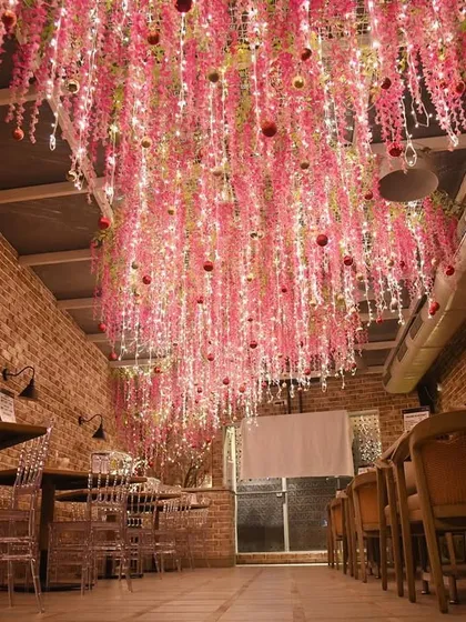A wide view of the pink floral Christmas ceiling. The exposed brick walls provide a rustic contrast to the whimsical, glowing installation.