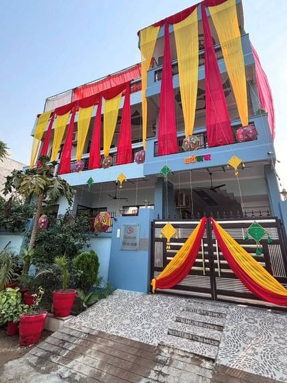 A daytime view of a house decorated with red and yellow drapes for a wedding. The entrance gate is also decorated to create a cohesive and festive look.
