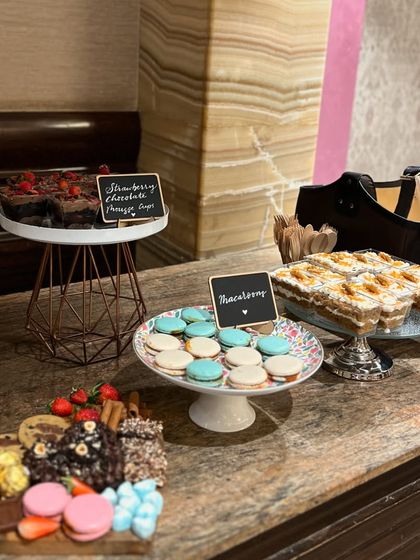 A close-up of the dessert table, highlighting the macarons, carrot cake slices, and strawberry chocolate orange cake.