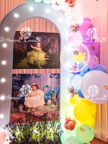 A personalized photo display featuring a lighted arch and a cascade of colorful balloons. This setup provides a beautiful way to showcase cherished photos of the birthday girl's first year.
