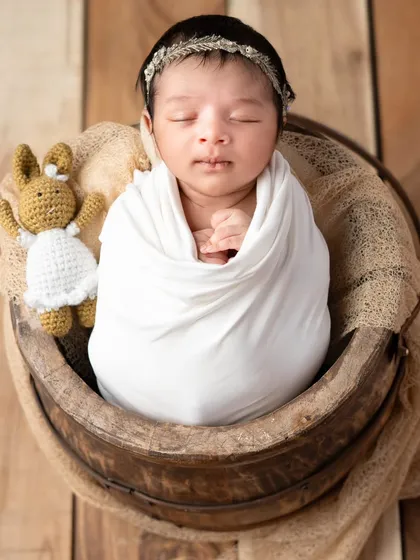 A classic pose in a rustic wooden bucket, with a tiny knitted friend for company. The natural tones and textures create a warm and earthy feel for this newborn photo.