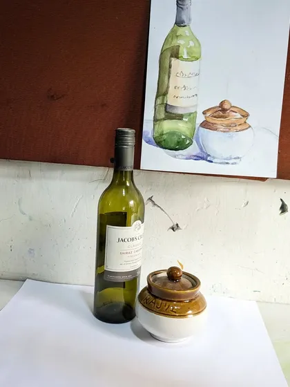 A still life setup of a wine bottle and a pickle jar, next to a student's beautiful watercolor rendition.