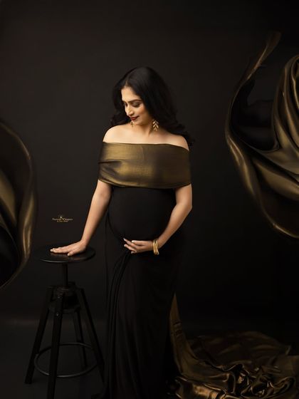 A graceful portrait of an expecting mother in a black and gold gown. The flowing fabric and her elegant pose create a look of timeless sophistication.