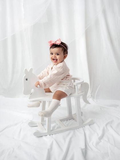 A playful shot of a baby girl on a white rocking horse. A classic and fun prop for a sitter session.