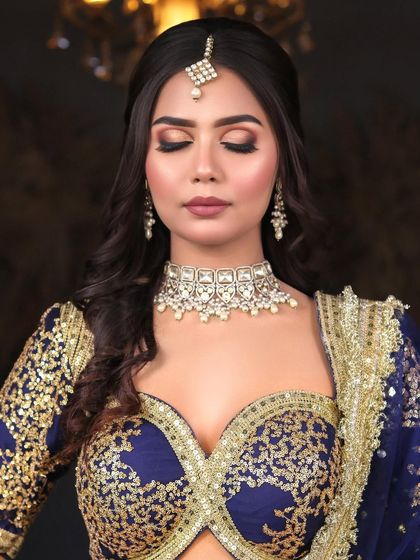 A beautiful engagement or reception look in a royal blue and gold lehenga. The makeup features a classic brown smokey eye and a flawless matte base.