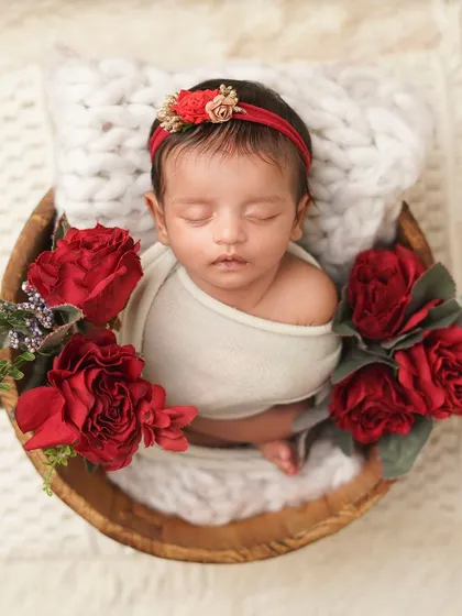 An overhead shot of a newborn in a wooden bowl, surrounded by rich red roses. This setup creates a romantic and classic feel for a baby girl's first photoshoot.