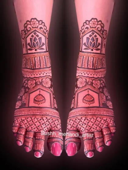 A symmetrical foot design with lotus motifs on the leg and jhumkas on the feet. The dark stain makes the intricate patterns stand out beautifully.