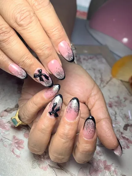 A chic French manicure with a black glitter ombre tip and a sophisticated 3D black bow accent.