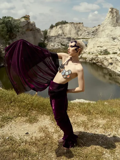 The flowing purple fabric creates a dynamic frame for the model, emphasizing the drama of the overall 'Siren' look.