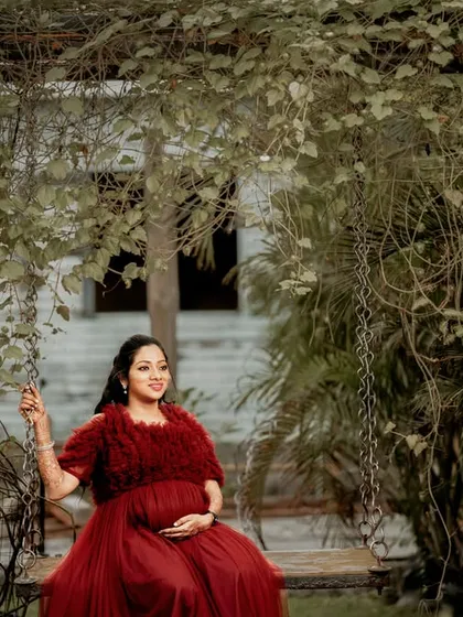 A peaceful solo portrait of an expecting mother in a flowing red gown, enjoying a quiet moment on a garden swing. This image showcases our ability to create elegant and timeless outdoor maternity portraits.
