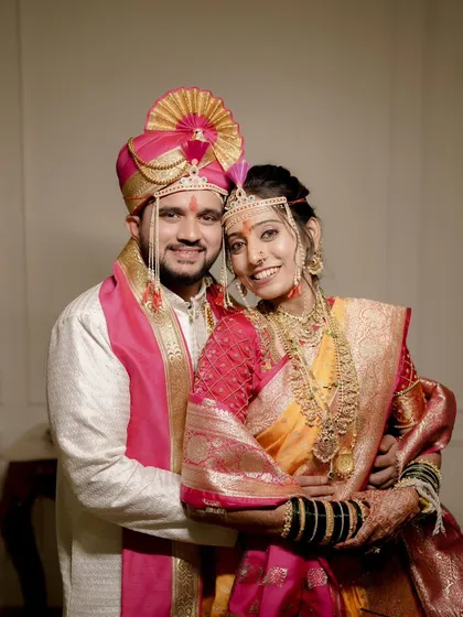 A classic portrait of the bride and groom. Her makeup features a warm, golden glow that beautifully complements her yellow and pink Paithani saree.