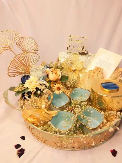 Looking for an exquisite gift hamper? This elegant tray features beautiful ceramic tea cups, a metal jar for snacks, and golden decorative elements, making it a luxurious choice for festive or corporate gifting.