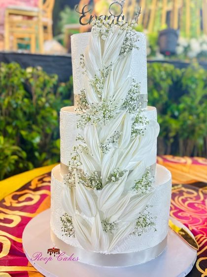 A closer look at the intricate wafer paper details on this stunning three-tier engagement cake, seen here at the event venue. The delicate textures and baby's breath create a truly breathtaking effect.