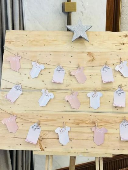 A creative way for guests to leave their wishes for the baby. We set up a rustic wooden board where notes written on baby onesie-shaped cards can be clipped, creating a charming and interactive display.