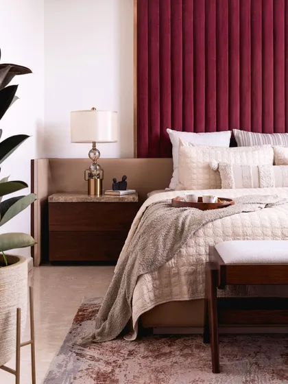 The deep red headboard contrasts beautifully with the neutral walls and soft, cream-colored bedding. A large plant adds a touch of nature and freshness to the room.