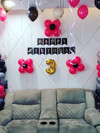 A modern birthday decoration for a three-year-old using a pink, grey, and black color scheme. The setup includes balloon columns and flower-shaped balloon clusters on the wall for a stylish and contemporary look.