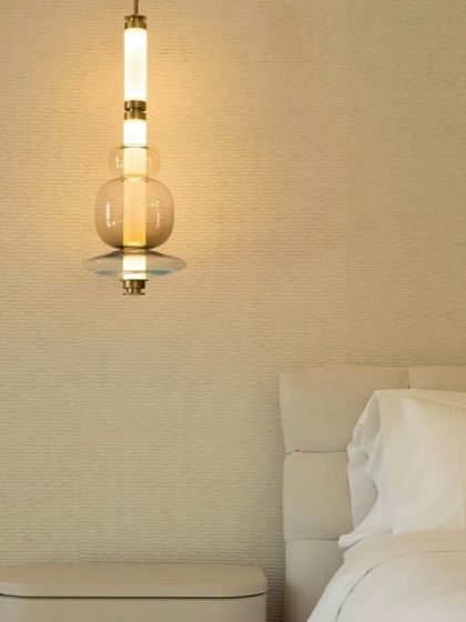 A single Luna pendant hangs beside a bed, providing focused light for reading while adding a touch of elegance to the room's decor.