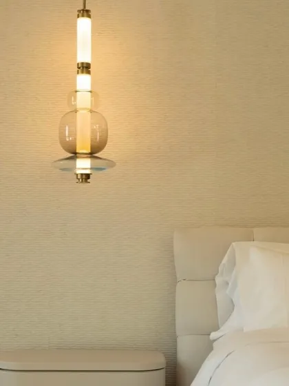 A detailed view of a single Luna Kaleido pendant next to a bed, highlighting the quality of the hand-blown glass and the warm, ambient light it produces.