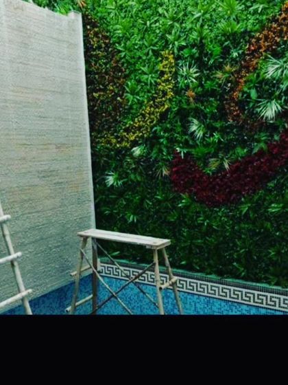 A work-in-progress shot of a custom design. This wall features a flowing pattern made with different colored foliage, including deep red and yellow, against a green background.