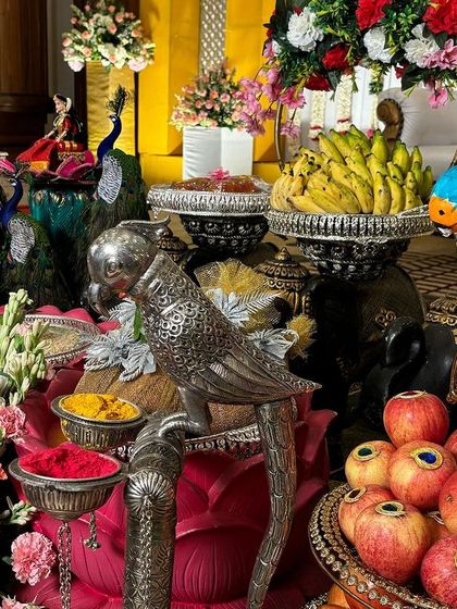 A colorful assortment of offerings, including fresh fruits, flowers, and silver parrot props.