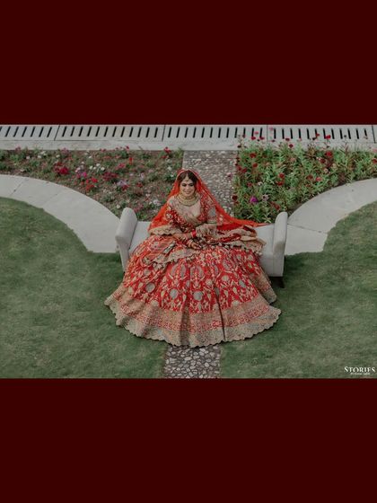 A regal portrait of the bride, Bhanvi, seated in her magnificent red lehenga, looking like royalty.