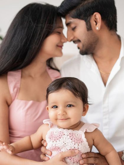 A close-up family portrait with the baby looking right at the camera, framed by her loving parents.