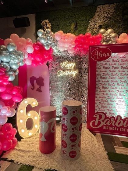 A glamorous Barbie-themed birthday party with a pink shimmer wall, a custom 'Barbie Edition' photo frame, and a balloon arrangement in shades of pink and silver.