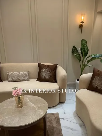 This view showcases the elegant wall paneling and warm wall lamps that add a touch of class to the living room. The peacock-feather-themed cushions on the sofa bring in a personalized, decorative element.