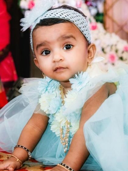 A close-up portrait of the baby girl at her naming ceremony, looking directly at the camera with her big, expressive eyes.