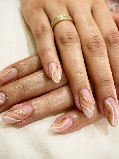 An elegant rose gold marble design, with delicate white and gold swirls over a sheer pink base on long, almond-shaped nails.