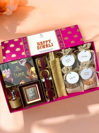 A closer look at the premium Diwali hamper, showcasing the rich textures and items. You can see the silver frame, gourmet treats from Smoor, and assorted dry fruits in jute potlis, all arranged in a beautiful pink designer box.