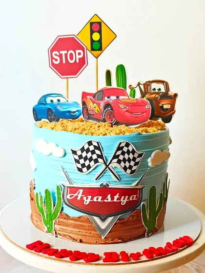 A Disney Cars-themed cake featuring Lightning McQueen and Mater in a desert scene. The "sand" is made from crushed biscuits, adding a fun texture to this exciting design.