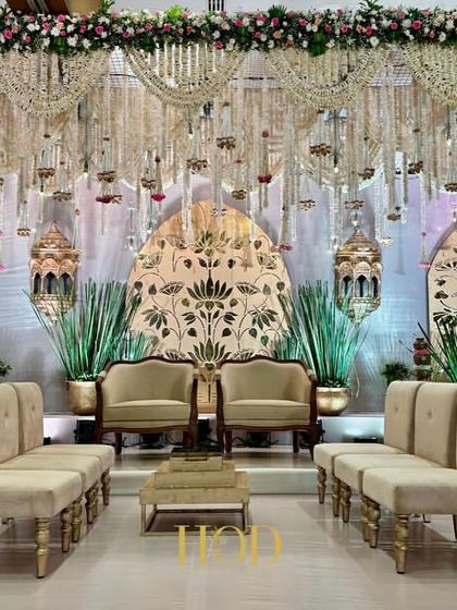 A closer look at a grand wedding stage, with intricate golden backdrops, elegant seating, and a ceiling dripping with traditional floral hangings.