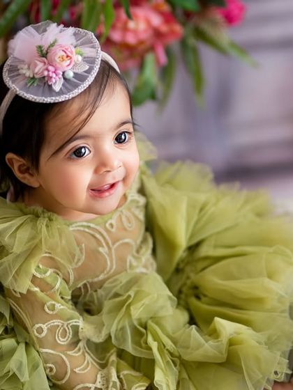 A close-up portrait capturing the delicate details of the outfit and the baby's bright, curious eyes during her first birthday tea party session.