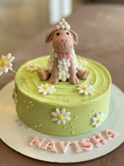 A sweet lamb cake for Navisha, set in a field of fondant daisies. The lamb figure is crafted with detailed "wool" texture.