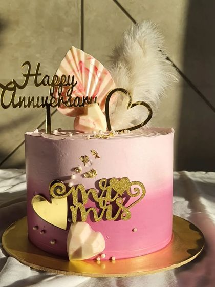 Simple aesthetic cakes are always a hit. This anniversary cake has a beautiful pink ombre design, topped with a chocolate sail, a feather, and gold heart toppers.