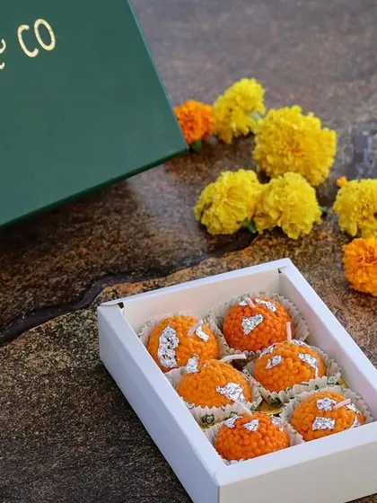 A box of six perfectly crafted Laddoo candles, presented in our elegant Mandy & Co. packaging next to fresh marigold flowers.