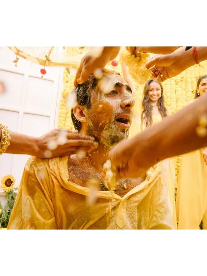 A groom gets doused with milk and turmeric during his haldi. The sheer chaos and his expression of surprise make this a classic, colorful, and energetic wedding moment.