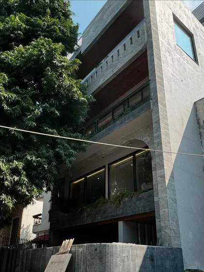 This multi-story residence in West End is nearing completion. The facade features a raw concrete finish, stone cladding, and large arched openings, creating a modern and monumental presence that still feels connected to the surrounding greenery.