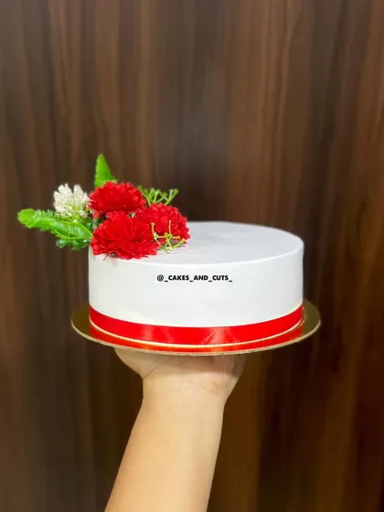 A minimalist cake with a red ribbon and simple red and white flowers.