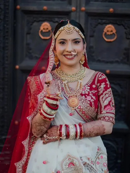 A beautiful portrait of the bride in her red and white lehenga. The makeup is designed to be graceful, with defined eyes and a lip color that complements her traditional attire.