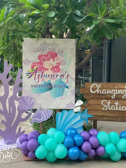 Welcome to Ashmira's Mermaid Bash. The entrance features a custom welcome sign, coral props, and a balloon garland in shades of purple and teal.