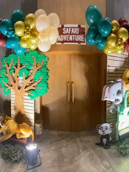 A safari adventure entrance featuring a jeep cutout filled with plush animals and a wooden tree prop, all framed by balloon clusters. This sets the perfect tone for a jungle party.