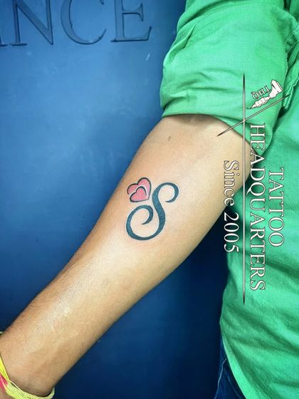A simple yet elegant initial "S" tattoo with two small hearts, perfect for a minimalist and personal statement.