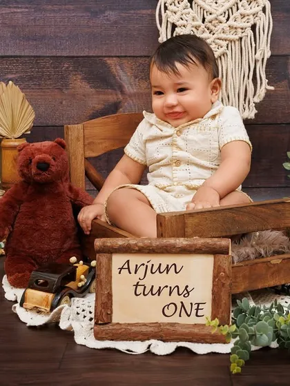 "Arjun turns ONE." A personalized portrait of a baby boy in a rustic, boho-themed setup for his first birthday.