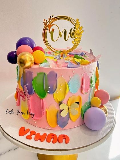 Sweet hues and tasty views on this colorful first birthday cake, decorated with abstract buttercream strokes and butterflies.